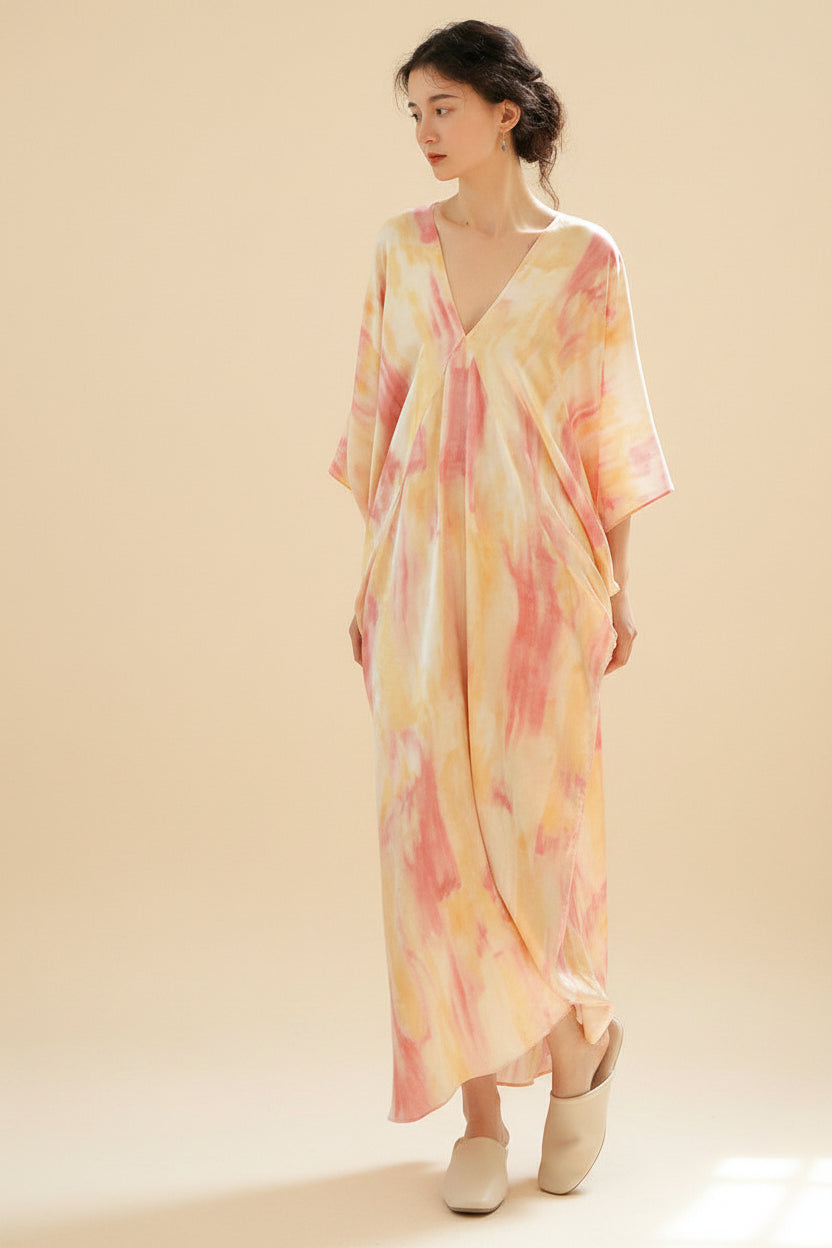 Woman wearing a tie-dye dress standing in a room with wooden furniture.
