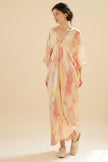 Woman wearing a tie-dye dress standing in a room with wooden furniture.